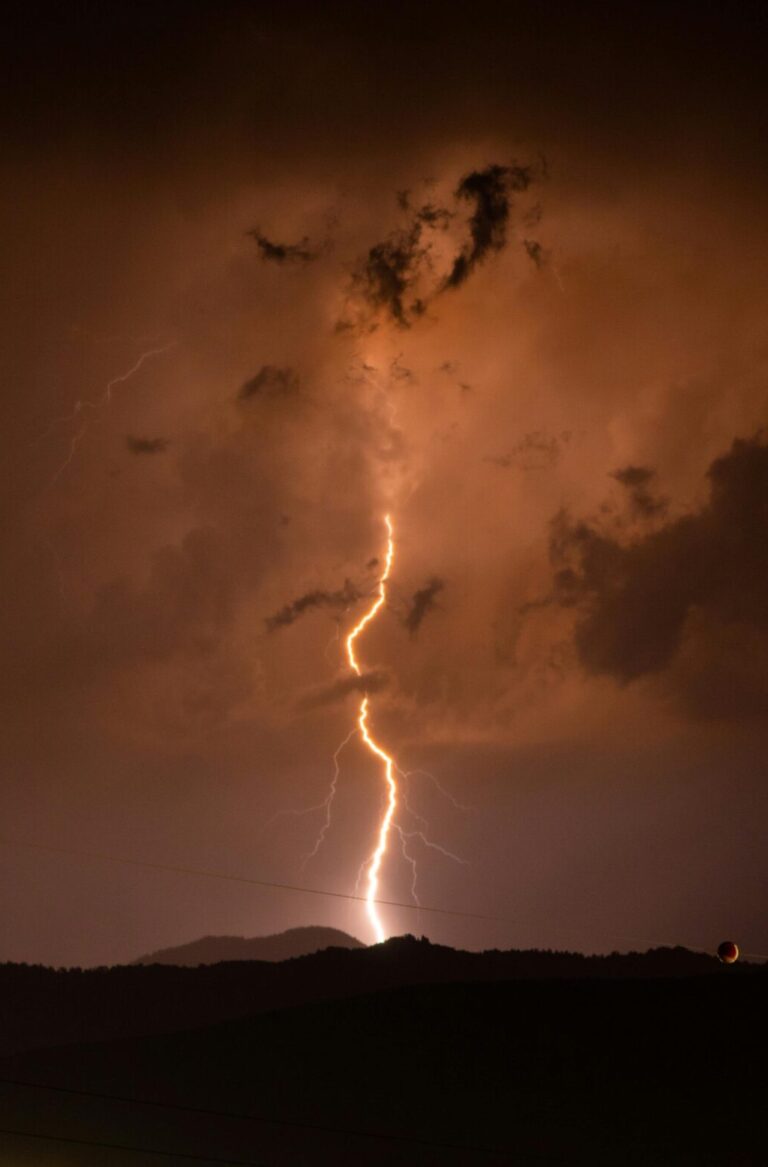 Éclair frappant le sol sous un ciel d'orage orangé, la nuit